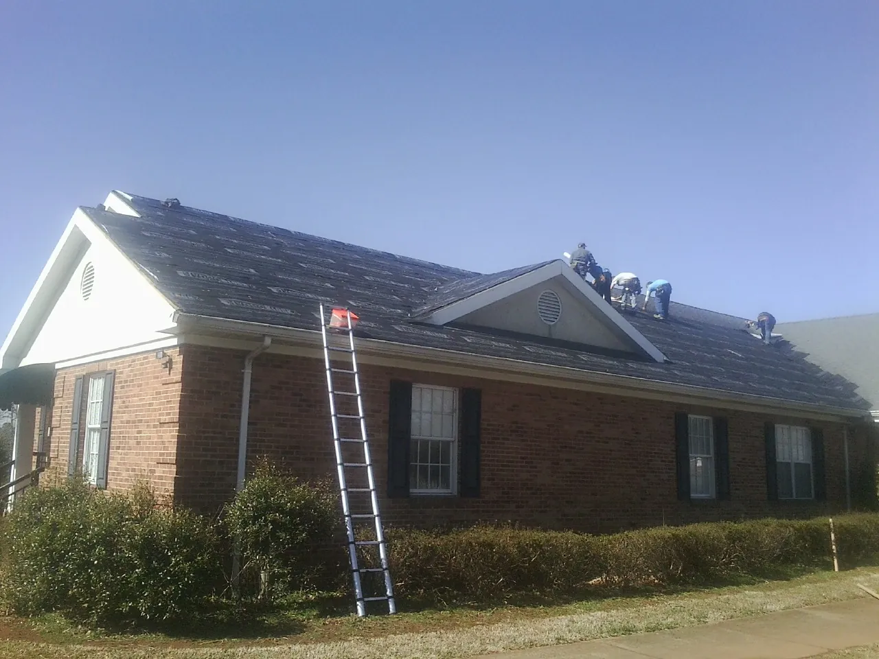 Crew tearing shingles off a brick ranch roof with a ladder set — Metal Roof Repair work by our crew in Garnerville