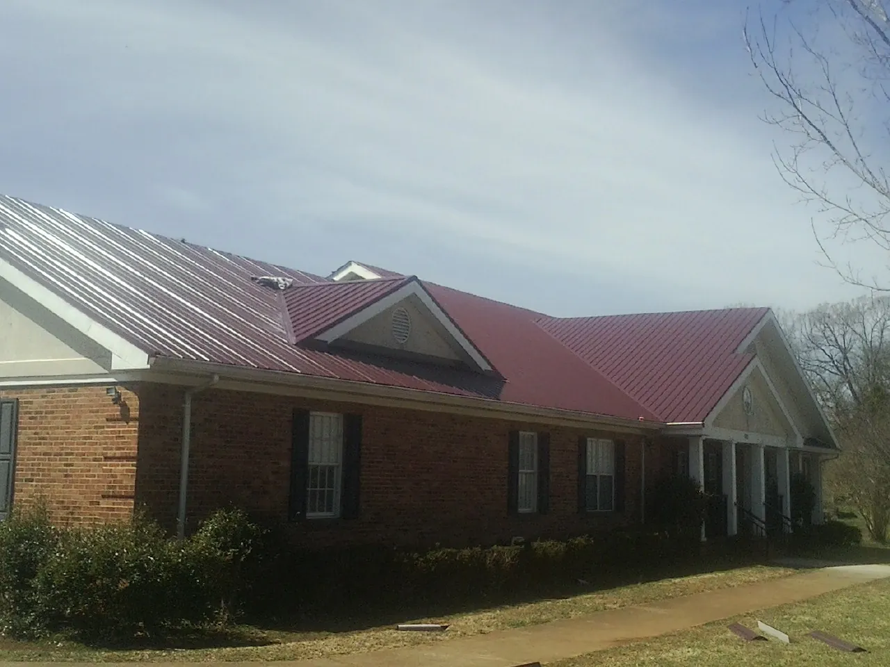 Red metal roof with gabled entries on a long brick building, from a Hail Damage Roof Repair job in Garnerville