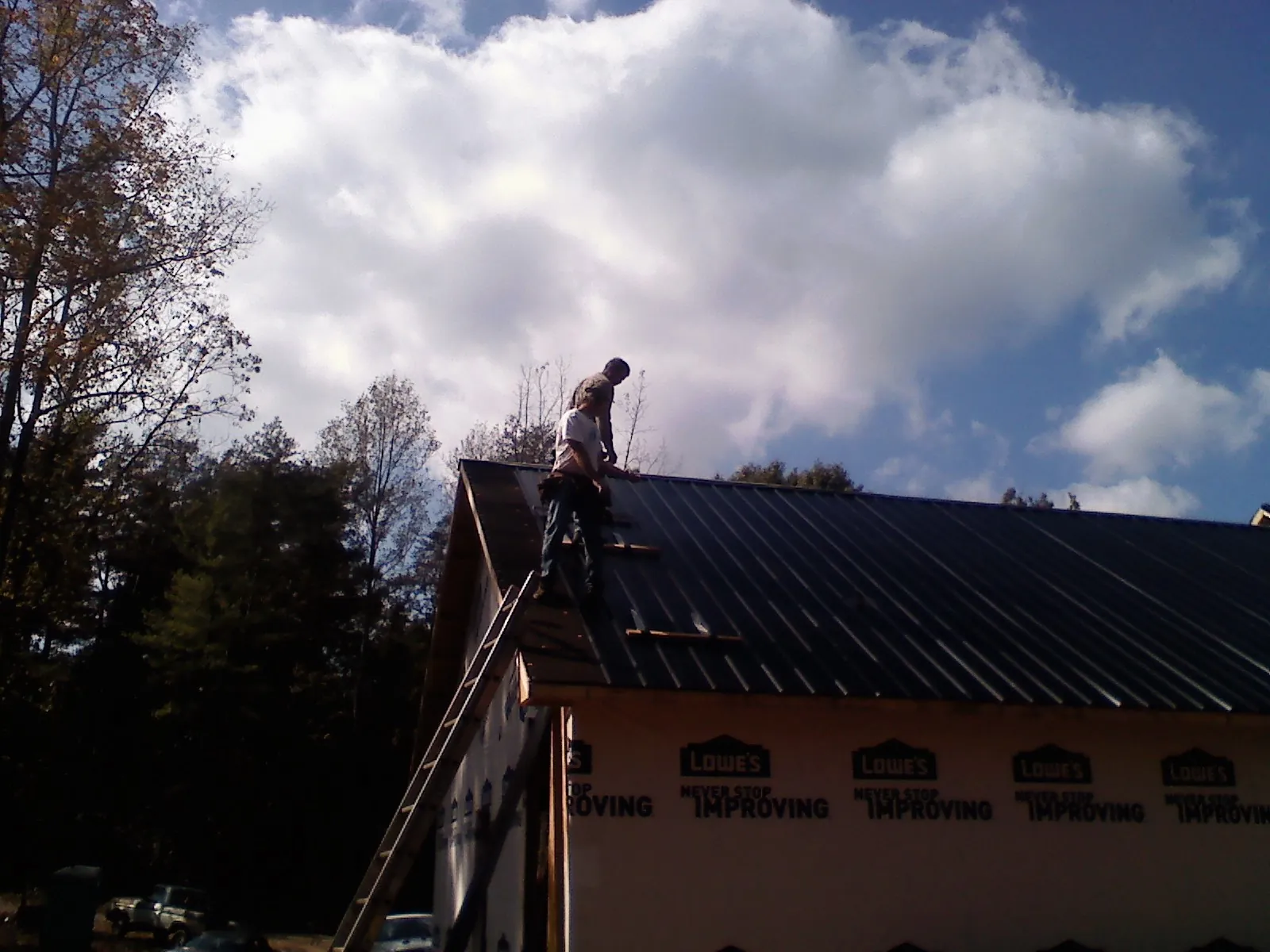Roofer fastening dark metal panels high against a cloudy sky, from a Roof Inspection job in Garnerville